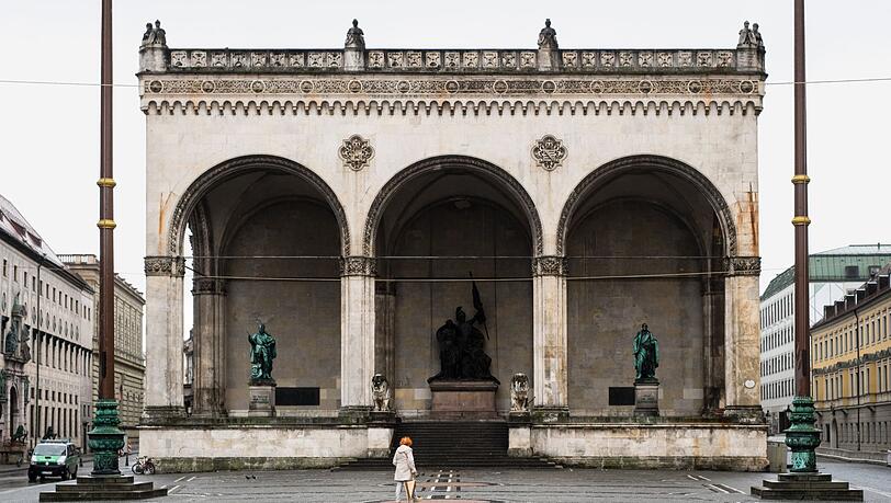Eine Frau geht über den menschenleeren Odeonsplatz an der Feldherrnhalle vorüber. Am Donnerstag soll dort das Projekt "Die Rückkehr der Namen" seinen Abschluss finden. Eine Frau geht über den menschenleeren Odeonsplatz an der Feldherrnhalle vorüber. Am Donnerstag soll dort das Projekt "Die Rückkehr der Namen" seinen Abschluss finden.