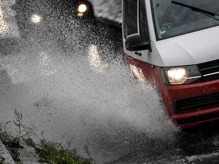 Autos fahren durch Starkregen auf einer Straße. Foto: Britta Pedersen/Archiv