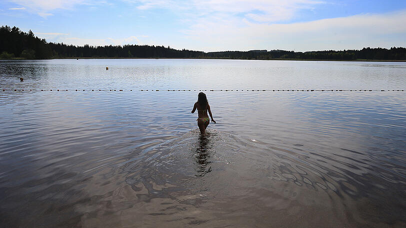 Eine Frau geht zum Schwimmen in das noch kühle Moorwasser des Elbsees in Aitrang.
