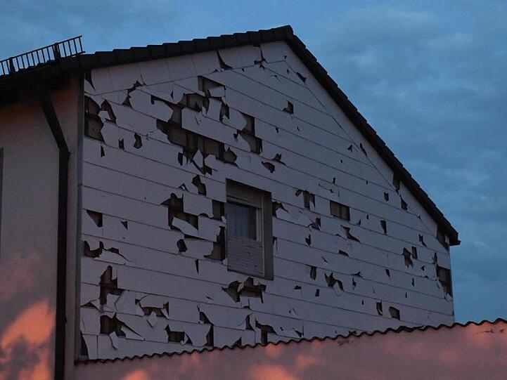 Eine durch Hagel bei einem Unwetter beschädigte Verkleidung einer Hauswand ist in der Abenddämmerung zu sehen. Foto: Felix Hörhager