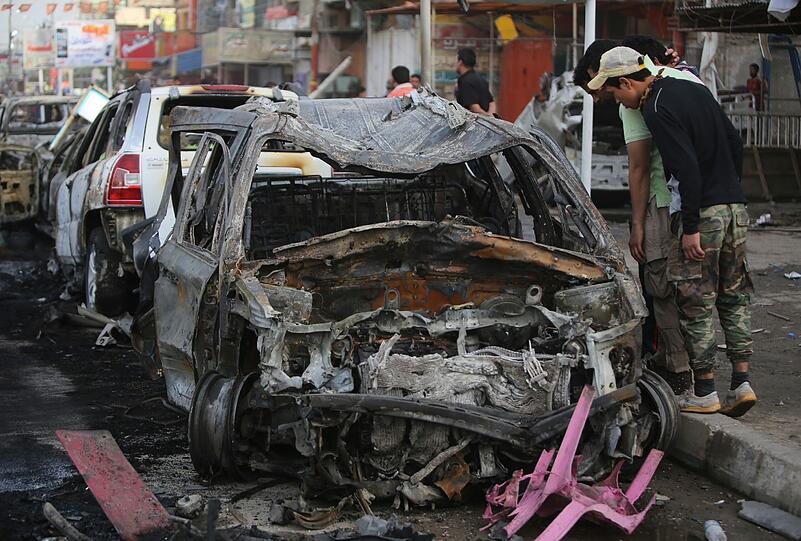 In Baghdad begutachten irakische Bürger die zerstörten Trümmer eines Autos nach einer Bombenexplosiion in einem schiitischen Wohnviertel.