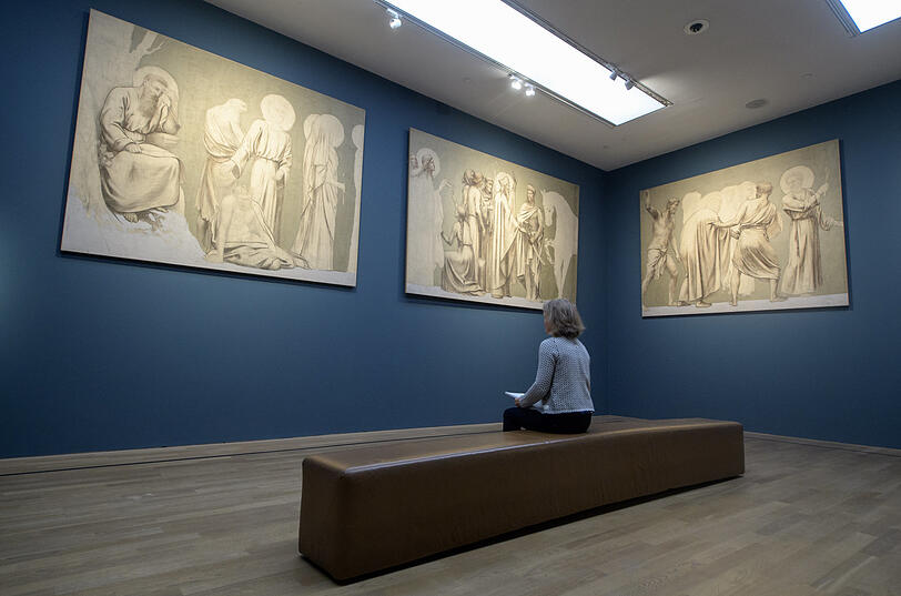 Eine Frau betrachtet am 21.09.2017 die Gemälde „Heiligenfiguren“ von Pierre Puvis de Chavannes in der Ausstellung „Gut. Wahr. Schön. Meisterwerke des Pariser Salons aus dem Musée d'Orsay“ in der Kunsthalle in München (2017).