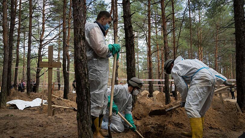 Arbeiter stehen auf dem Waldfriedhof von Isjum am Grab eines nicht identifizierten Zivilisten. Dort wurden nach Angaben aus Kiew mehr als 400 Leichen gefunden. Die Menschen sollen ums Leben gekommen sein, als Russland die Stadt Ende März beschoss.