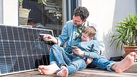 Ein Vater sitzt mit Kind auf einer Terrasse und zeigt auf ein großes Solarpanel.
