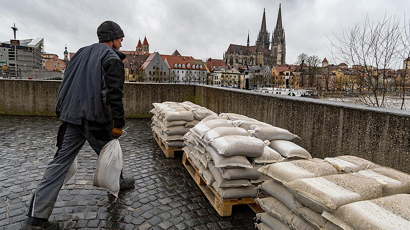 Ein Mann trägt am Donnerstag am Ufer der Donau in Regensburg Sandsäcke. Der Hochwassernachrichtendienst rechnete mit einem weiteren Anstieg der Pegelstände.