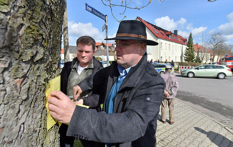 Der zurückgetretene Bürgermeister von Tröglitz, Markus Nierth (r), heftet in der Nähe eines ausgebrannten Hauses (Hintergrund) in Tröglitz einen Aufruf zu einer Kundgebung an einen Baum.