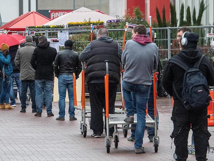 Vor einem Baumarkt stehen Menschen in einer Schlange.
