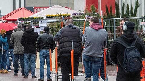 Vor einem Baumarkt stehen Menschen in einer Schlange.