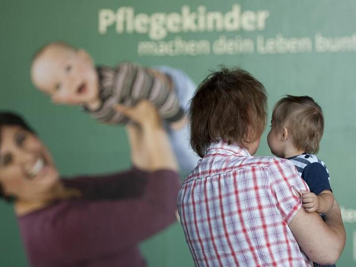 Eine Frau steht nach einer Pressekonferenz des Kinder- und Jugendhilfe-Verbundes mit ihrem Pflegekind vor einem Plakat. Foto: Marc Tirl/Archiv