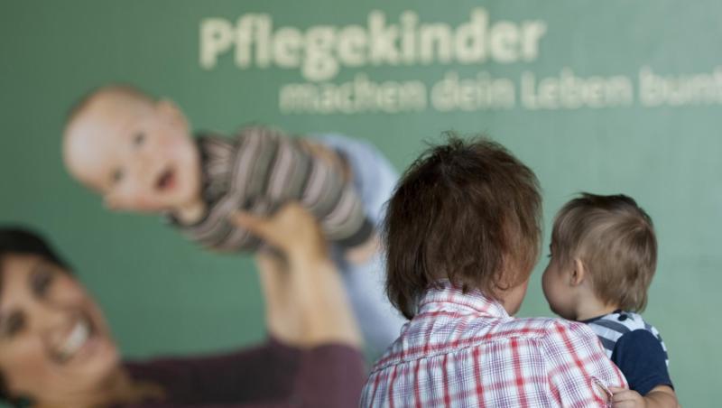 Eine Frau steht nach einer Pressekonferenz des Kinder- und Jugendhilfe-Verbundes mit ihrem Pflegekind vor einem Plakat. Foto: Marc Tirl/Archiv Eine Frau steht nach einer Pressekonferenz des Kinder- und Jugendhilfe-Verbundes mit ihrem Pflegekind vor einem Plakat. Foto: Marc Tirl/Archiv