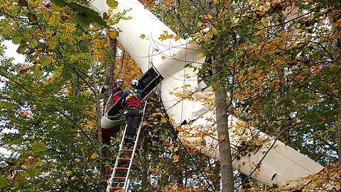 Mitarbeiter der Bergwacht stehen während Bergungsarbeiten an einem Segelflugzeug auf einer langen Leiter.