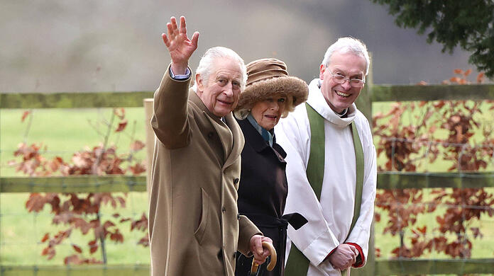 König Charles winkt den Fotografen in Sandringham zu.