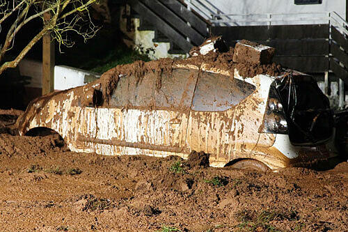 Ein Auto steckt nach dem Erdrutsch tief im Schlamm.
