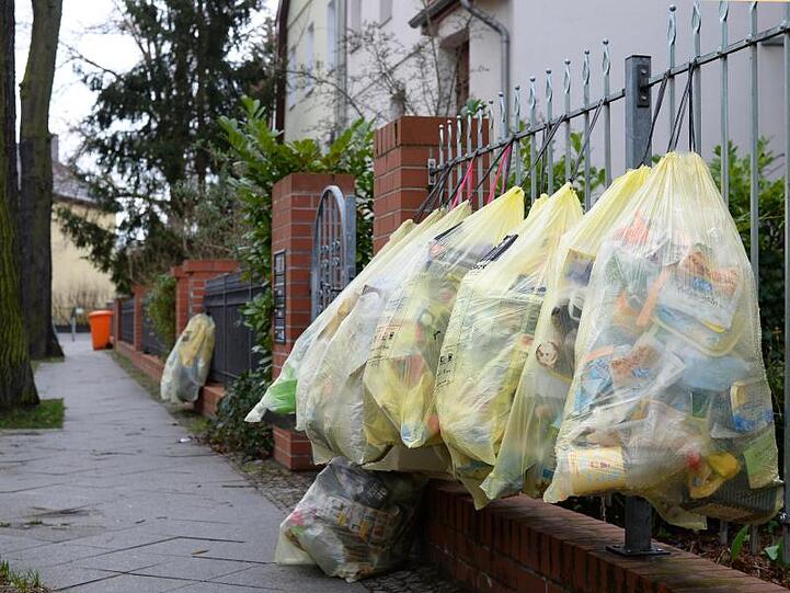 Gefüllte gelbe Müllsäcke hängen in einer Straße am Gartenzaun zur Abholung bereit.