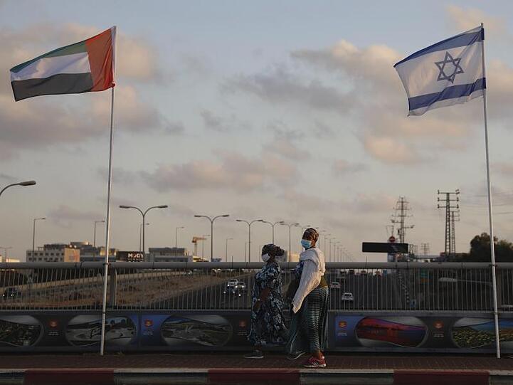 Frauen mit Schutzmasken gehen an den Flaggen von Israel und den Vereinigten Arabischen Emiraten auf der Friedensbrücke im israelischen Netanya vorbei.
