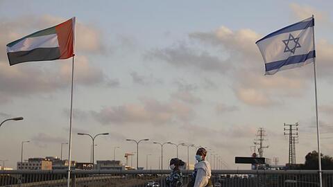 Frauen mit Schutzmasken gehen an den Flaggen von Israel und den Vereinigten Arabischen Emiraten auf der Friedensbrücke im israelischen Netanya vorbei.