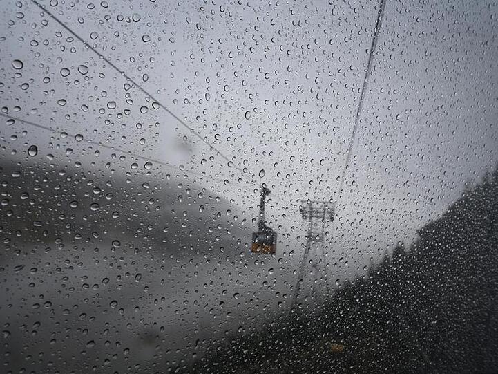 Eine Gondel der Nebelhornbahn fährt hinter der Fensterscheibe einer anderen Gondel durch den Regen. Foto: Karl-Josef Hildenbrand/dpa