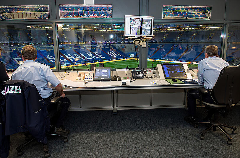 Zwei Polizeibeamte sitzen in der Polizei-Leitstelle der Videoüberwachung in der Veltins Arena. Von hier werden alle Bereiche im Stadion mittels Videoüberwachung kontrolliert.