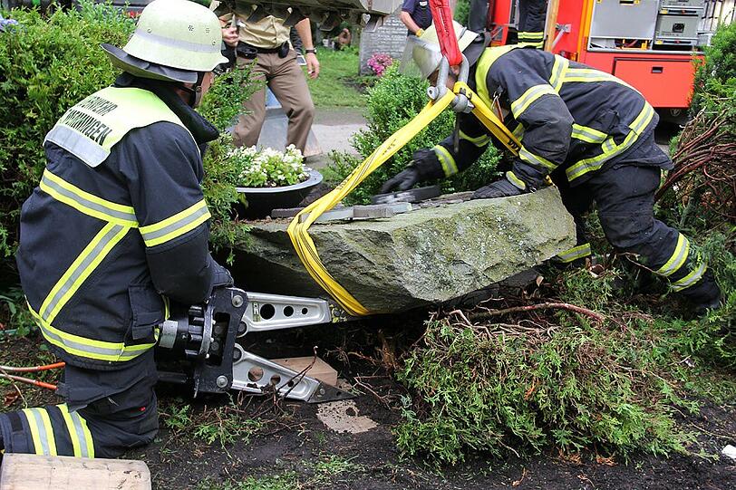 Feuerwehrmänner heben den umgefallenen Grabstein am Memminger Waldfriedhof mit einem Hydraulikspreizer hoch.