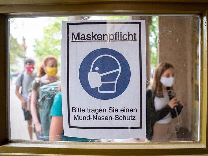 Schüler betreten hinter einem Plakat mit der Aufschrift "Maskenpflicht" am ersten Tag nach den Sommerferien den Eingang ihres Gymnasiums.