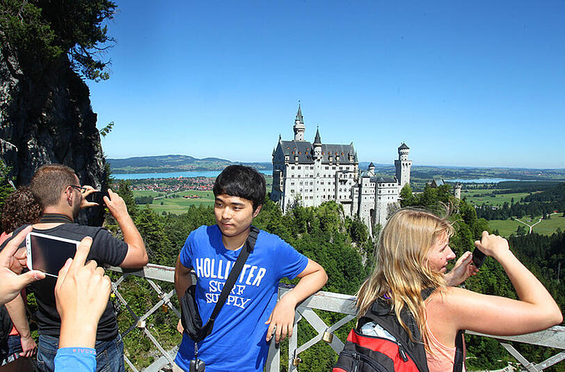 Touristen knipsen von der Marienbrücke aus Erinnerungsfotos mit Schloss Neuschwanstein im Hintergrund.