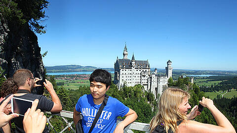 Touristen knipsen von der Marienbrücke aus Erinnerungsfotos mit Schloss Neuschwanstein im Hintergrund.