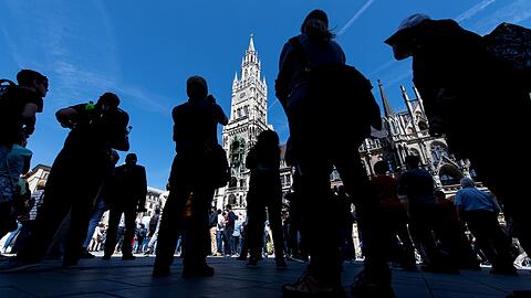 Touristen und Einheimische verfolgen das Glockenspiel auf dem Marienplatz in München.