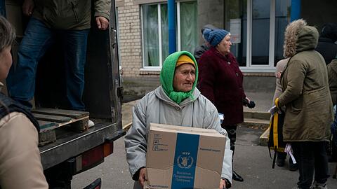 Eine ältere Frau trägt eine Kiste, während in dem Dorf Mychajlo-Lukaschewe humanitäre Hilfsgüter verteilt werden.