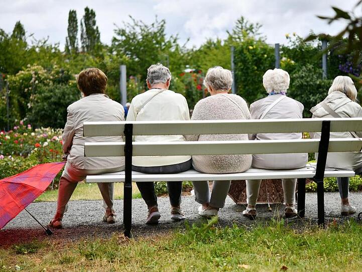 Fünf ältere Frauen machen nach einem Regenschauer eine Pause auf einer Parkbank.