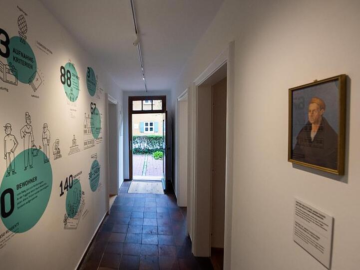 In der Fuggerei hängt ein Porträt von Jakob Fugger gegenüber einer Wand, auf der Zahlen und Fakten aufgemalt sind. Foto: Stefan Puchner