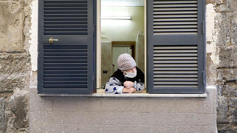 Eine ältere Frau schaut aus dem Fenster ihrer Wohnung. (Symbolbild)