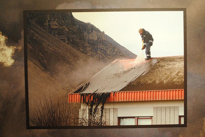 Ein Arbeiter spült die Ascheschicht des Eyjafjallajökull vom Dach des Bauernhauses. Foto aus dem Museum