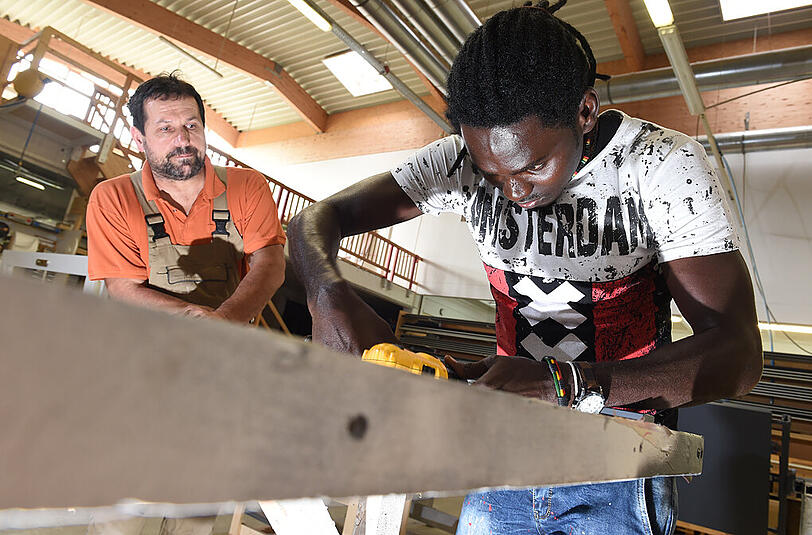 Ausbildung als großer Schritt zur Integration: Asylbewerber Omar Ceesay (r) arbeitet in einer Schreinerei in Baden-Württemberg an einer Tür. Schreiner Karl-Heinz Kübler schaut dem künftigen Lehrling zu.