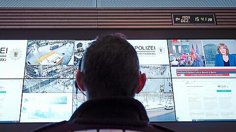 Ein Beamter hält im Führungs- und Lagezentrum des Polizeipräsidiums in Mannheim vor einer Wand mit Bildschirmen die Lage im Blick.