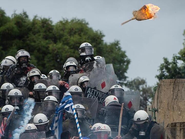 Ein brennender Strohbesen fliegt auf Bereitschaftspolizisten zu, die in Athen von Demonstranten attackiert werden.