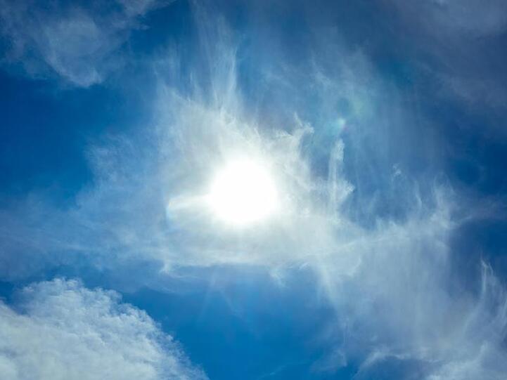 Die Sonne scheint am blauen Himmel durch Wolken hindurch. Foto: Markus Scholz/dpa/Archivbild