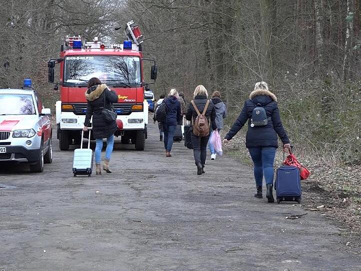 Bahnreisende ziehen ihre Rollkoffer über eine Straße bei Rheine. 200 Reisende mussten wegen einer gesperrten Bahnstrecke in Busse umsteigen.