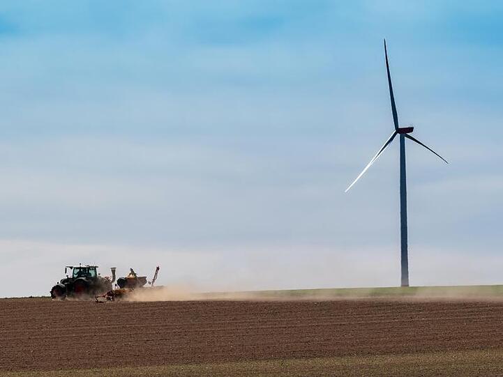 Ein Traktor fährt über einen trockenen Acker in Bayern und zieht eine Staubwolke hinter sich her.
