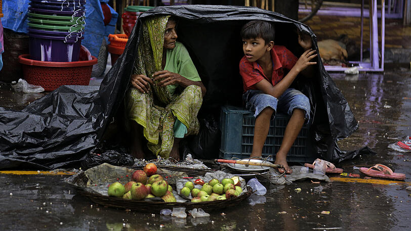 29.07.2018, Kolkata, Indien: Obsthändler schützen sich am Straßenrand mit einer Plane vor dem Regen. Die Monsunsaison in Indien dauert von Juni bis September.