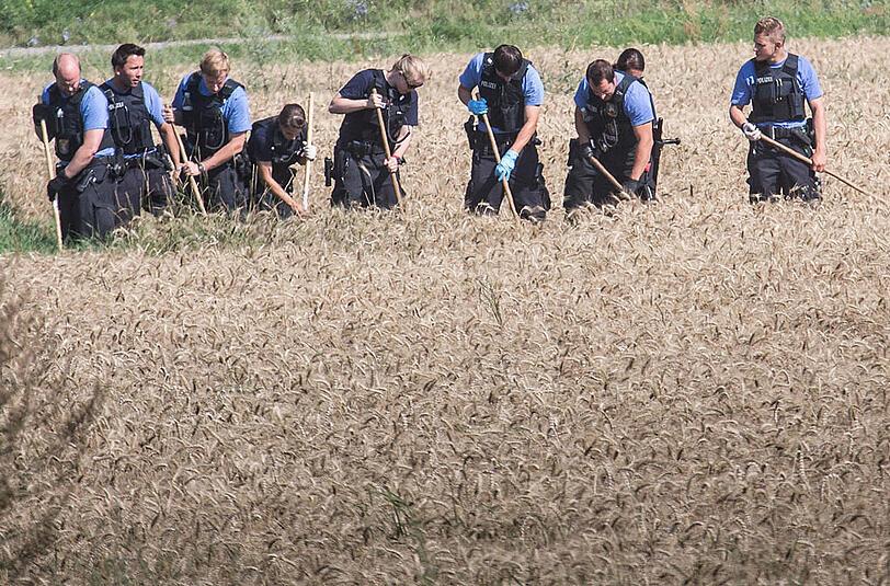 Polizisten durchkämmen am 24.07.2014 in Bischofsheim im Kreis Groß-Gerau (Hessen) ein Kornfeld in unmittelbarer Nähe des Tatorts, an dem am Abend zuvor ein Polizist erschossen wurde.