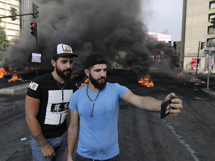 Zwei Teilnehmer einer Demonstration fotografieren sich vor einer brennenden Straßenblockade mit einem Smartphone.