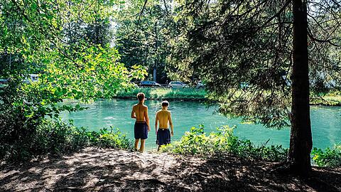 Zwei Burschen haben sich ein ruhiges Platzerl am Isarwerkkanal bei Thalkirchen gesichert und ihre Handtücher ausgebreitet. Langsam tasten sie sich ins kalte Wasser – bei der Hitze fällt das Eintauchen in die Isar besonders schwer. Ein paar Meter weiter scheint die Kälte schon vergessen: Eine Gruppe junger Buben schwingt an einem Seil in den Kanal und hat dabei eine heiden Gaudi.