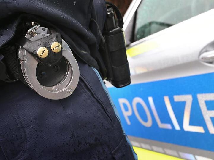 Ein Polizist mit Handschellen und einer Pistole am Gürtel steht vor einem Streifenwagen. Foto: Karl-Josef Hildenbrand/Archivbild