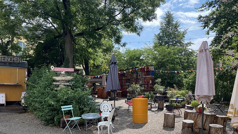 Das Café Steinchen: Pflanzen so weit das Auge reicht und bunt zusammengewürfelte Möbel. Im Hintergrund steht der Bauwagen-Kiosk. Das Café Steinchen: Pflanzen so weit das Auge reicht und bunt zusammengewürfelte Möbel. Im Hintergrund steht der Bauwagen-Kiosk.