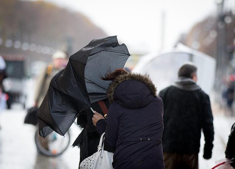 Eine Passantin kämpft mit dem Wind um ihren Regenschirm.