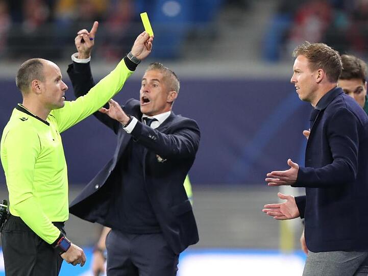 Schiedsrichter Antonio Mateu Lahoz (l) zeigt Leipzigs Trainer Julian Nagelsmann (r) die Gelbe Karte, dahinter gestikuliert Lyons Trainer Sylvinho.
