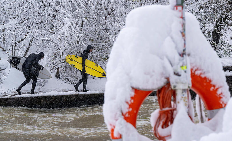 Zwei Männer gehen bei eisigen Temperaturen mit ihren Surfbrettern am Eisbach im Englischen Garten entlang.