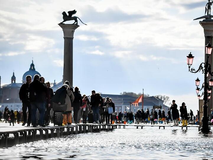 Touristen gehen über Stege, die über das Hochwasser führen.