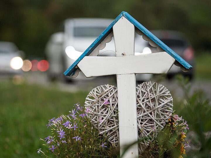 Autos fahren an einem weißen Kreuz für eine Unfalltote vorbei. Die Zahl der Todesopfer auf deutschen Straßen wird dieses Jahr voraussichtlich leicht steigen.