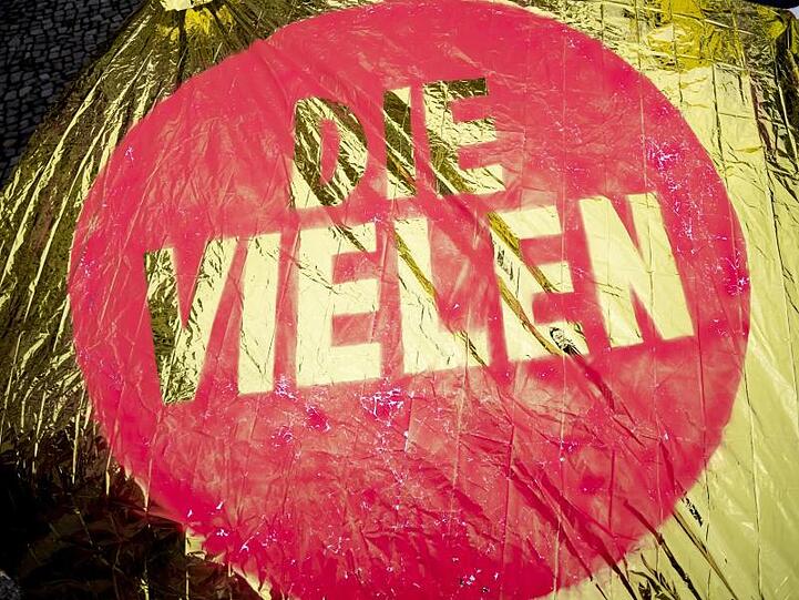 &bdquo;Die Vielen" steht auf einer glänzenden Fahne. Foto: Christoph Soeder/Archiv